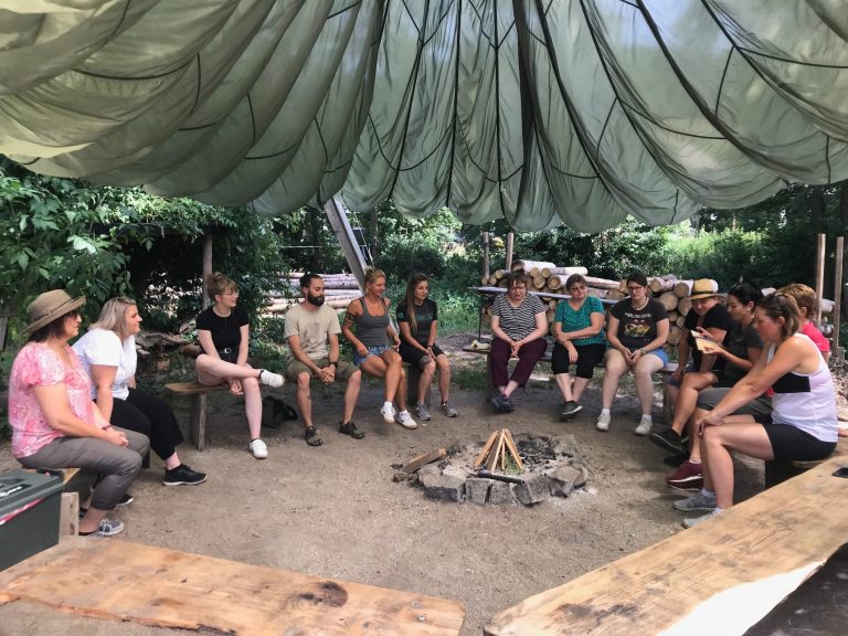 Gruppe sitzt um Feuerstelle in der Natur während einem Teamtag